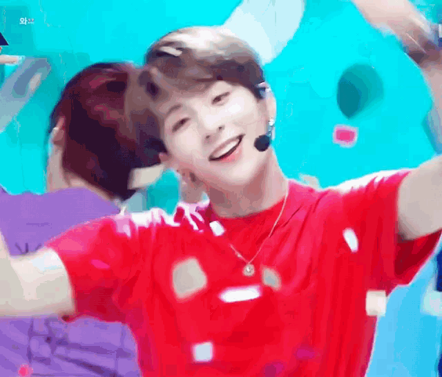 a young man wearing a red shirt and a necklace is smiling and looking at the camera