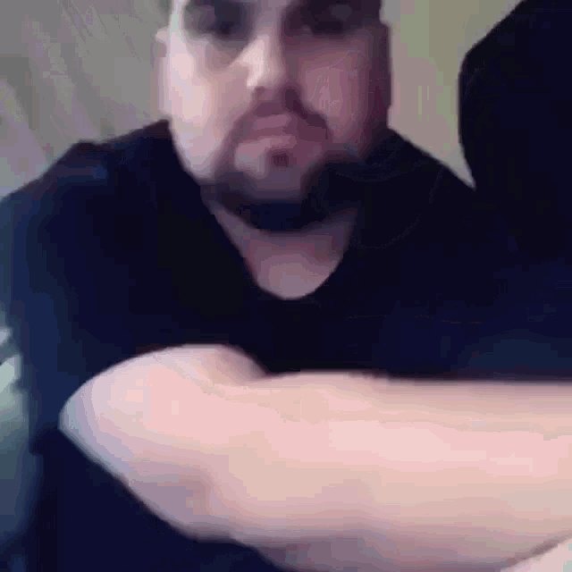 a man with a beard and a black shirt is holding his arms crossed .