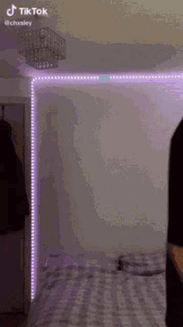 a person is standing in a bedroom with purple lights on the wall and a chandelier .