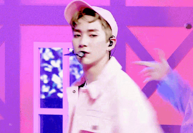 a man wearing a white hat and ear buds is standing in front of a pink and purple background