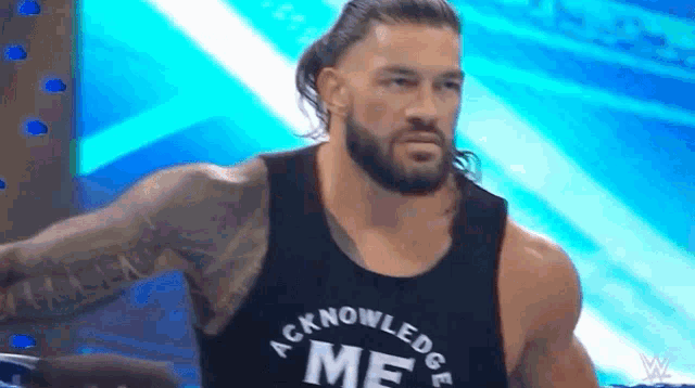 roman reigns is wearing a black tank top that says `` acknowledge me '' on it .