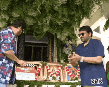 two men standing in front of a clapper board with the number 157 on it