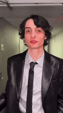 a young man wearing a black suit and tie
