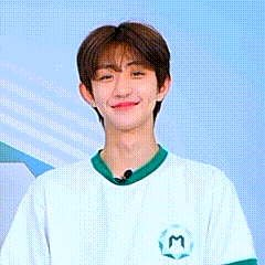 a young man wearing a white t-shirt with a green collar and a m on the back is smiling .