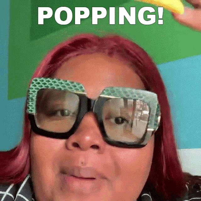 a woman with red hair is wearing sunglasses and holding a banana in front of a green background that says popping !