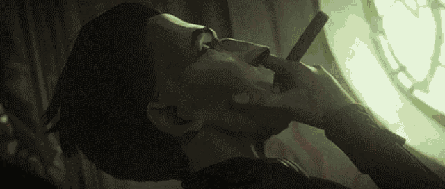 a man is smoking a cigarette in front of a window in a dark room .