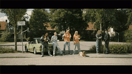 a group of people standing on a sidewalk with a green car in the background