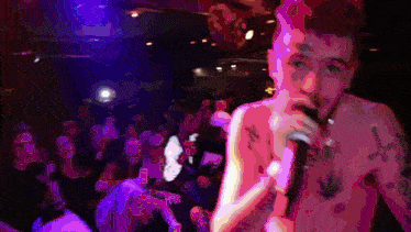 a shirtless man singing into a microphone in front of a crowd of people