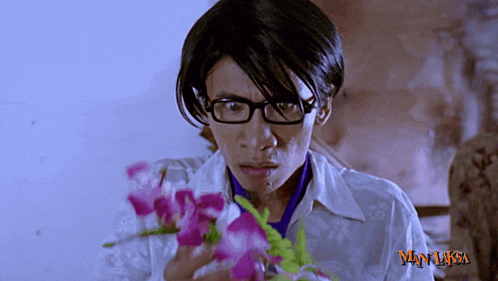 a man wearing glasses is holding purple flowers in front of a man laksa sign