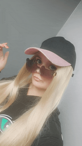a woman with long blonde hair wearing a black hat and pink sunglasses