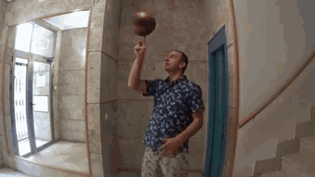 a man in a blue shirt is holding a basketball on his finger