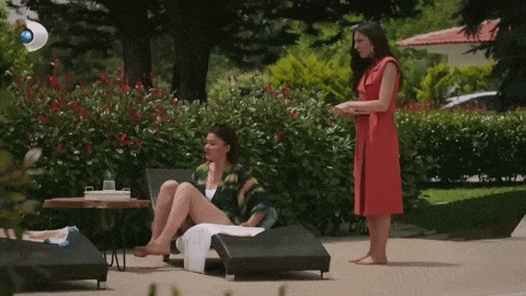 a woman in a red dress is standing next to a woman sitting on a lounge chair