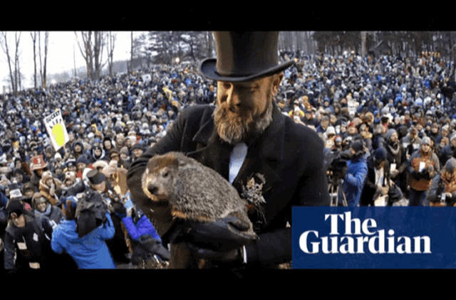 a man in a top hat is holding a groundhog in front of a crowd of people and the guardian logo in the corner
