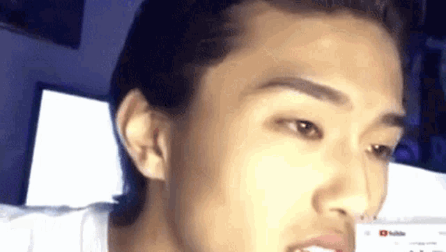 a close up of a young man 's face with his mouth open and a computer screen in the background .