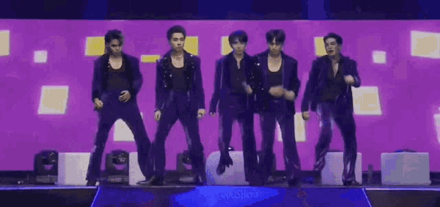 a group of men are dancing on a stage in front of a purple backdrop .