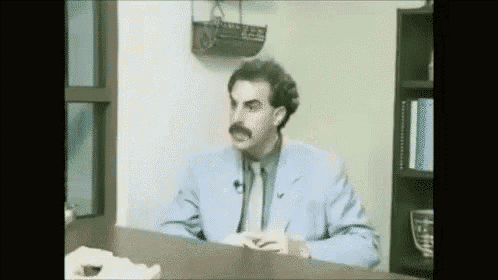 a man in a blue suit and tie is sitting at a desk in a room .