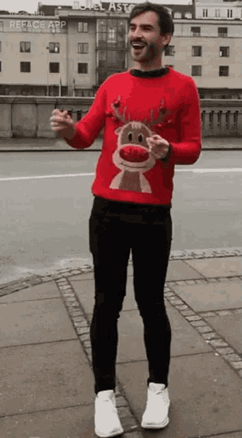 a man wearing a red sweater with a reindeer on it is standing on a sidewalk
