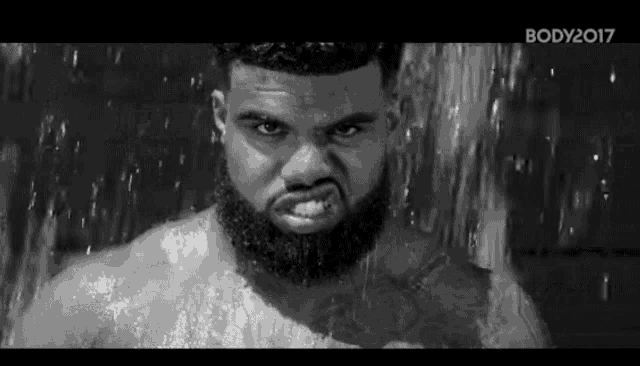 a black and white photo of a man with a beard taking a shower .