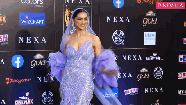 a woman in a purple dress is standing in front of a wall that says nexa gold on it