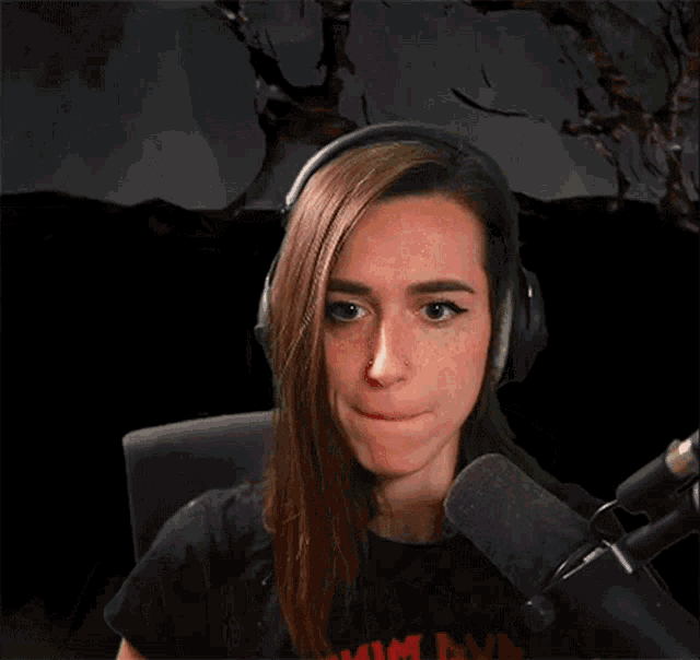 a woman wearing headphones and a black shirt is sitting in front of a microphone .