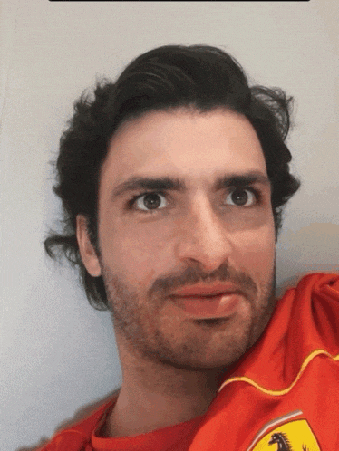 a man with a beard wearing a red shirt with a ferrari logo on it