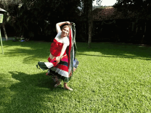 a woman in a red white and black dress is dancing in a park