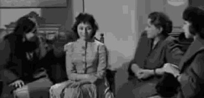 a group of women are sitting around a table talking to each other .