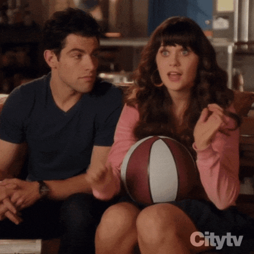 a man and a woman are sitting on a couch and the woman is holding a basketball in her lap