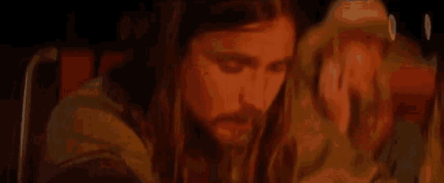 a man with long hair and a beard is sitting next to a woman in a chair .