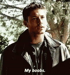 a man in a leather jacket is standing in front of a tree and talking about his breasts .