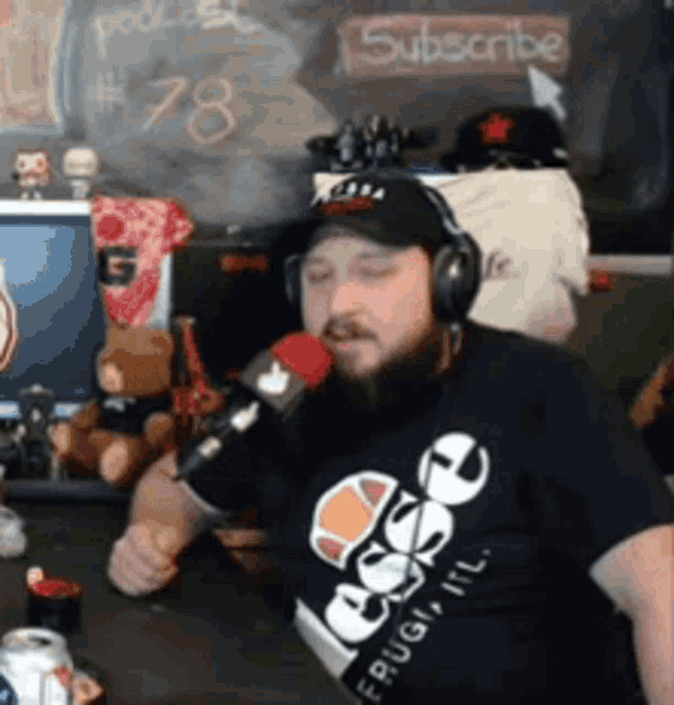 a man with a beard wearing headphones and an ellesse shirt is singing into a microphone
