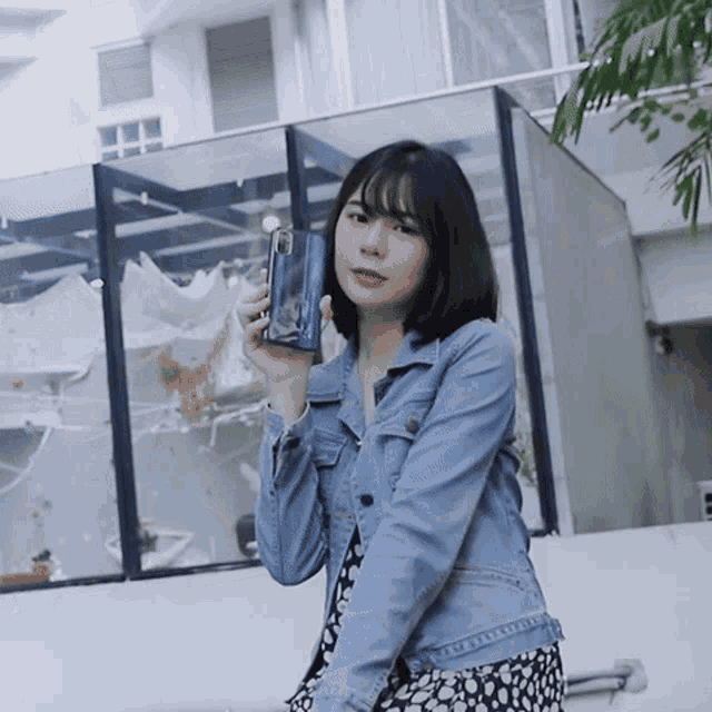 a young woman in a denim jacket is holding a cell phone