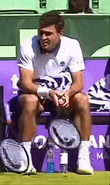 a man sits on a bench with a tennis racquet in front of a purple wall that says am