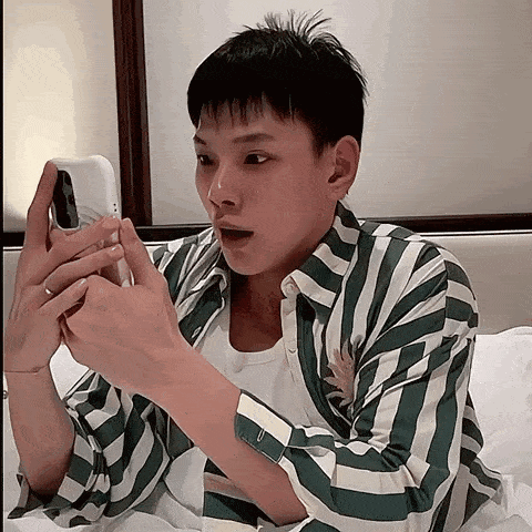 a man in a green and white striped shirt is using a cell phone