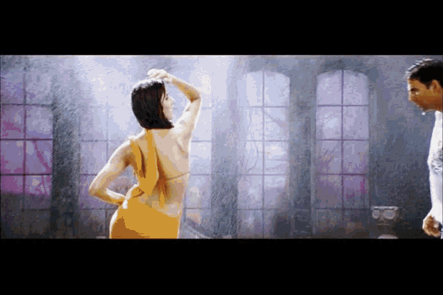 a woman in a yellow dress is dancing in the rain with a man