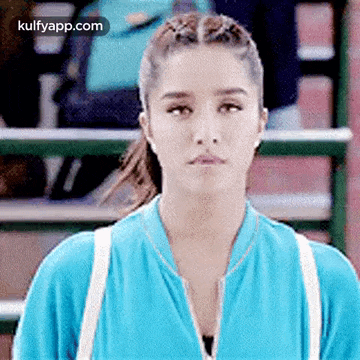 a woman in a blue jacket is looking at the camera while standing on a tennis court .
