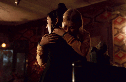 two women hugging each other in a dark room with a patterned wall