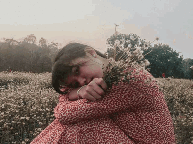 a woman in a red dress sits in a field holding a bouquet of flowers