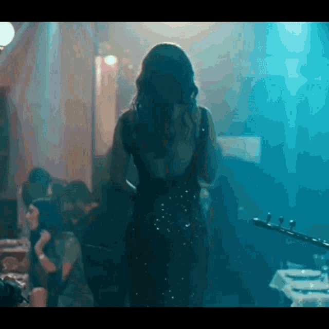 a woman in a black dress is standing in a dark room in front of a crowd .