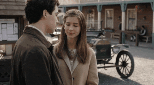 a man and a woman are looking at each other in front of a ford car