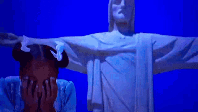 a little girl covering her face in front of a statue of jesus with ay madre written above her