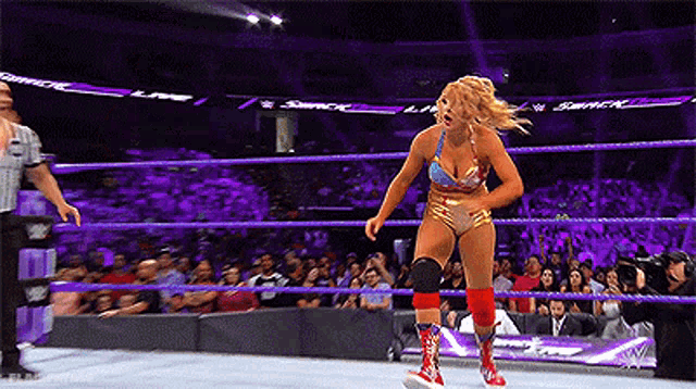 a woman is standing in a wrestling ring while a referee watches .