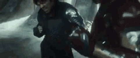 a man in a black jacket is fighting another man in a red suit in a dark room .