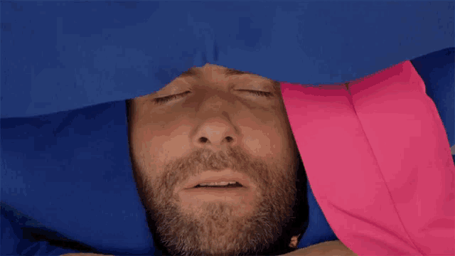 a man laying under a blue and pink blanket with his eyes closed