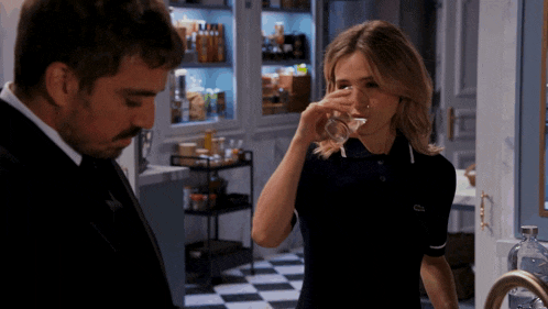 a man and a woman are standing in a kitchen and the woman is wearing a lacoste shirt