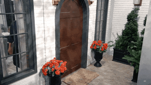 a front door with a wicker mat and red flowers in front of it