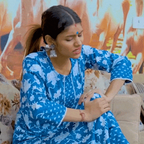 a woman in a blue dress is sitting on a couch with her hands on her knees