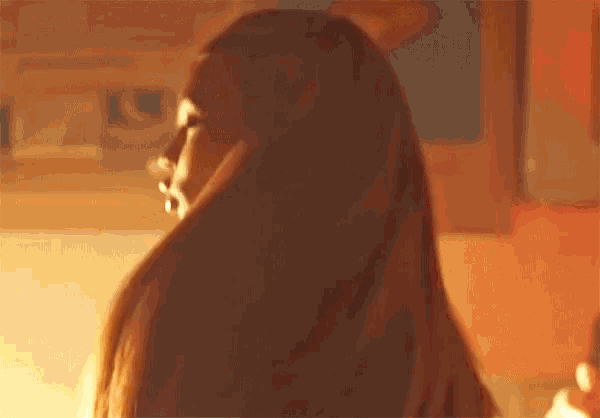 a woman with long hair is standing in a room with a blurred background .