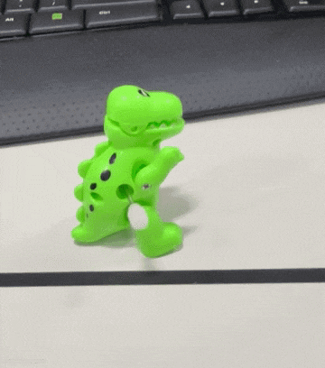 a green toy dinosaur is standing on a white surface .
