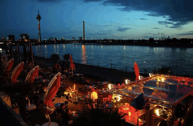 a group of people sitting at tables near a body of water at night